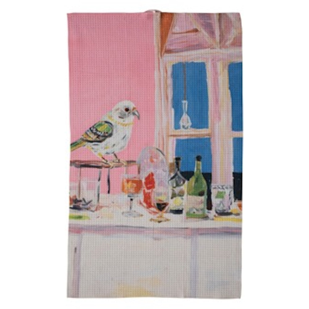 An artistic tea towel featuring a painted bird perched on a table with bottles and glasses against a pink and blue backdrop.