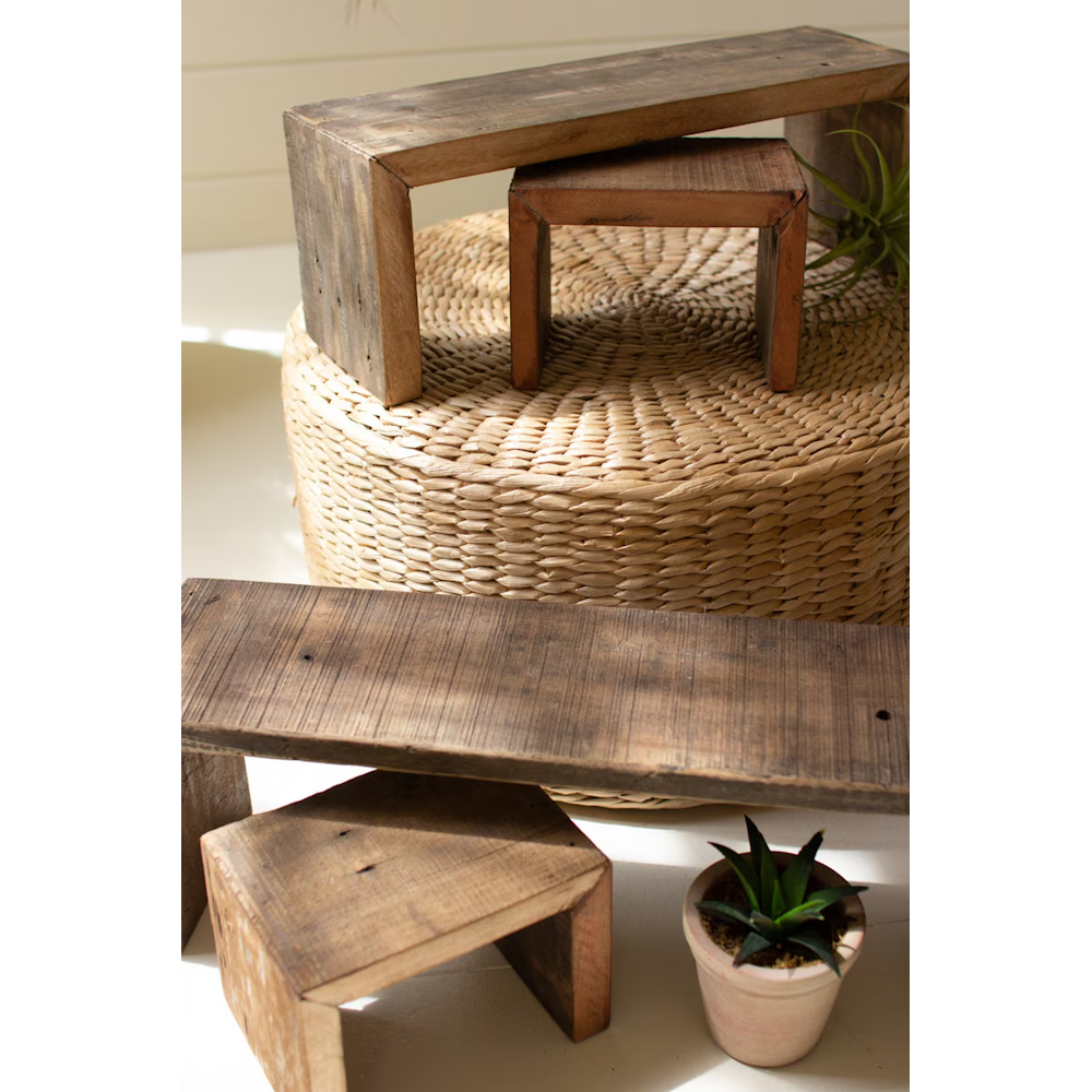Four rustic, recycled wood nesting risers in varying sizes arranged on and around a woven pouf.