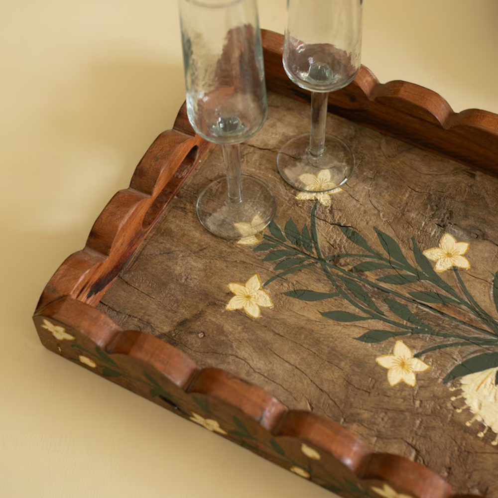 Close-up of a scalloped wooden tray hand-painted with white flowers, holding two clear glasses.