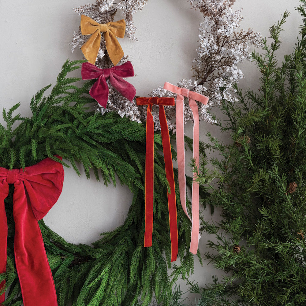 Various velvet bows in different colors decorating green and snowy holiday wreaths.