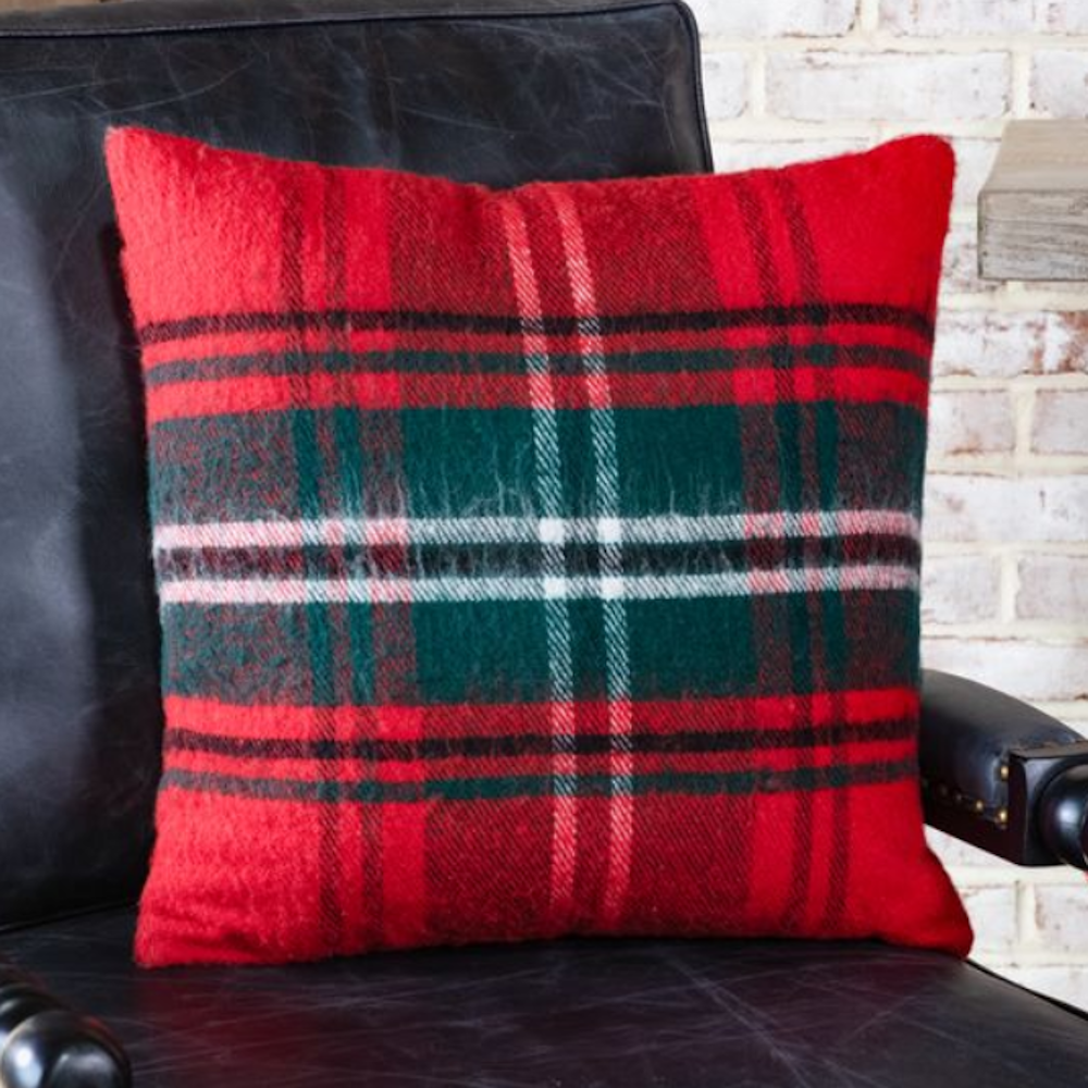 A square red tartan plaid throw pillow with green and white stripes resting on a black leather chair.