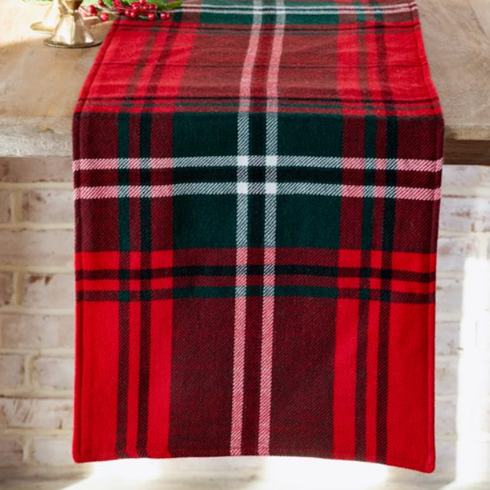 A red tartan plaid fabric table runner with green and white stripes draped over a wooden tabletop.