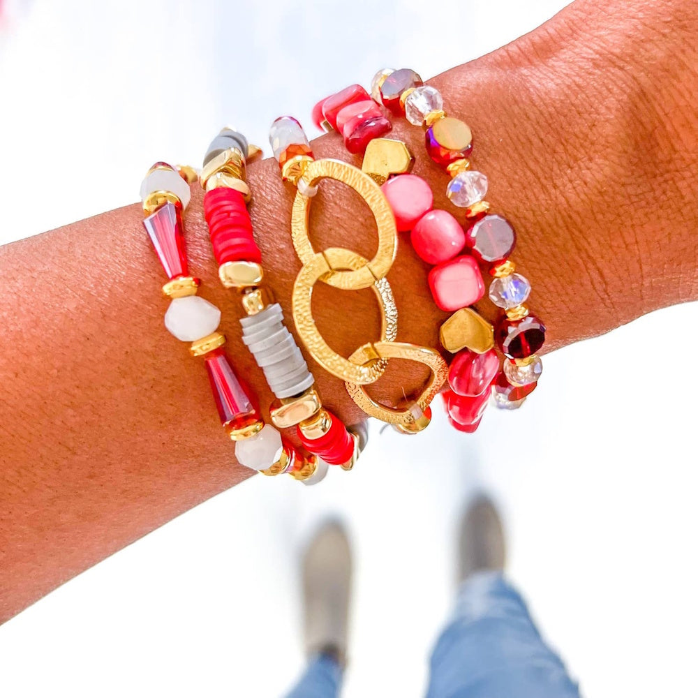 A stack of red, pink, grey, and gold beaded bracelets worn on a person's wrist.