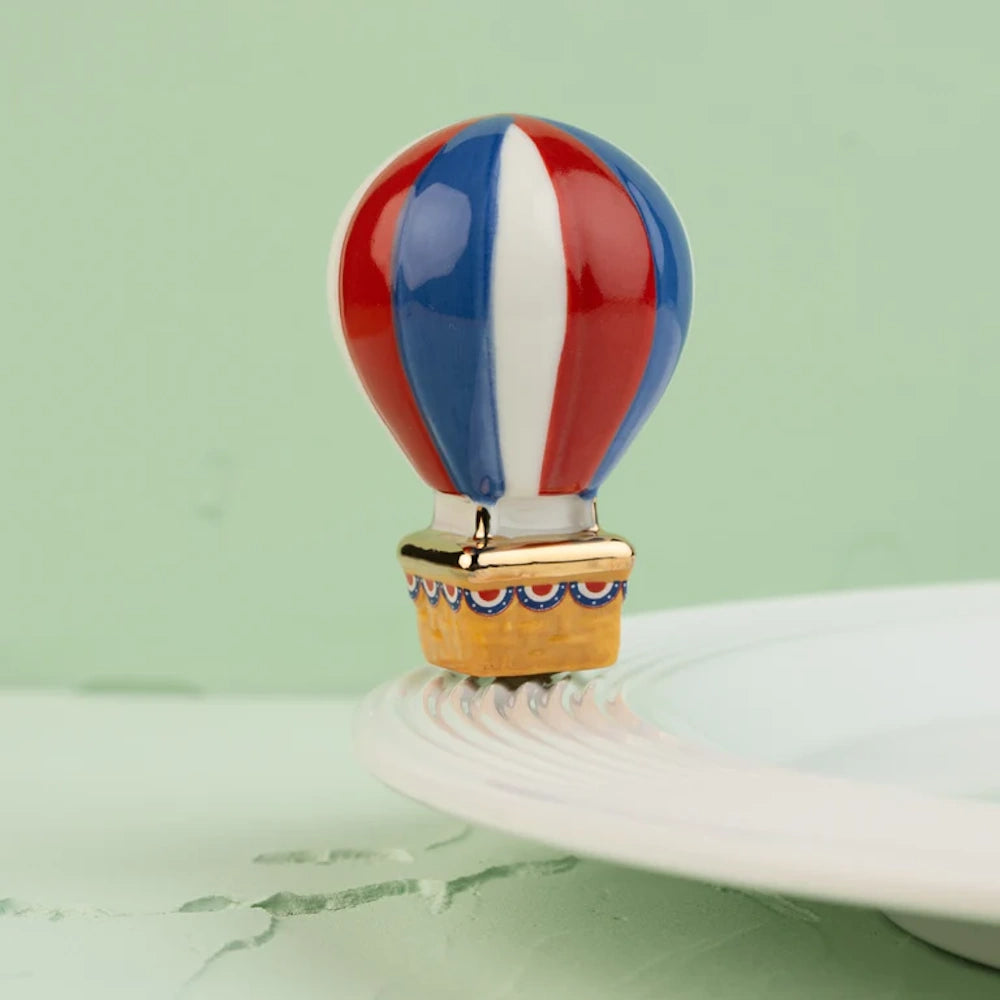 Red, white, and blue ceramic hot air balloon figurine sitting on the edge of a white serving plate.