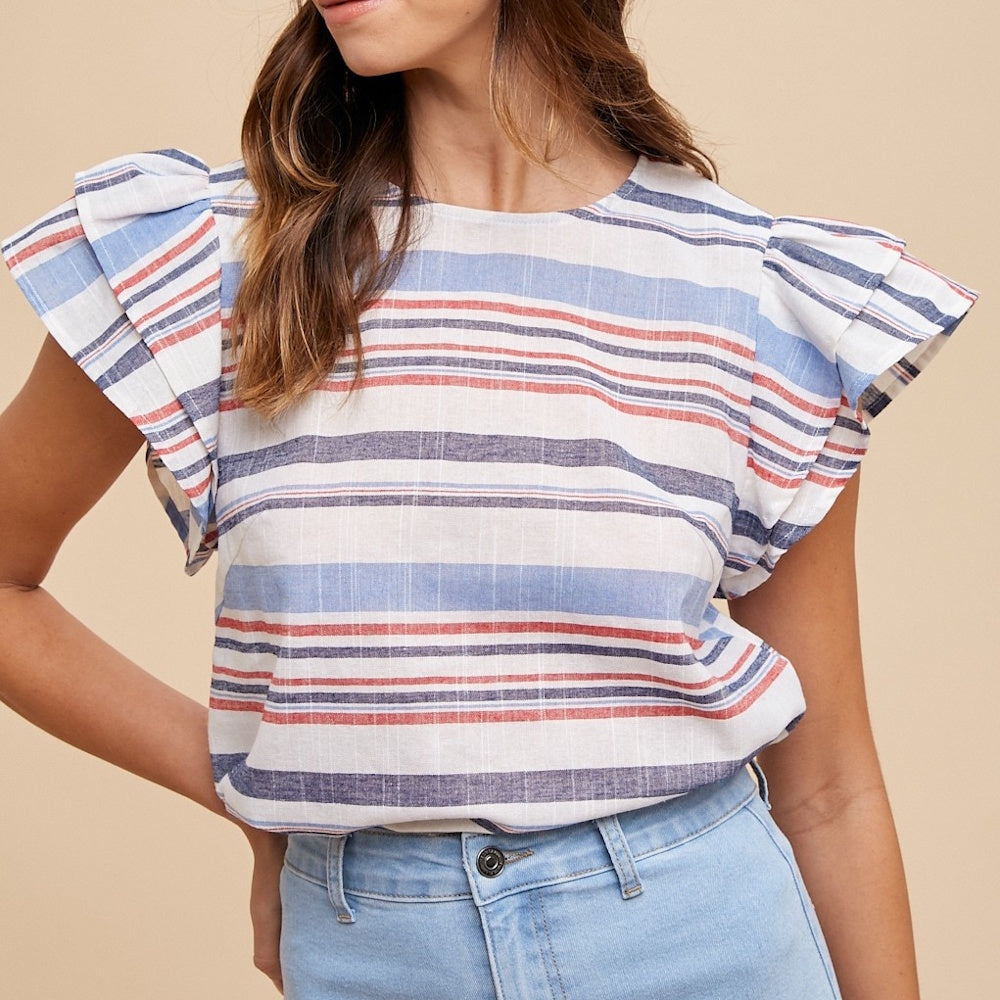 A woman wears a striped red, white, and blue blouse with short, tiered ruffle sleeves and light-wash jeans.