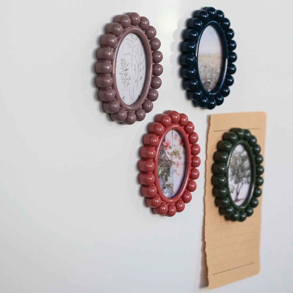 Colorful oval bobbin-style resin photo frame magnets with beaded edges displayed on a white refrigerator door.