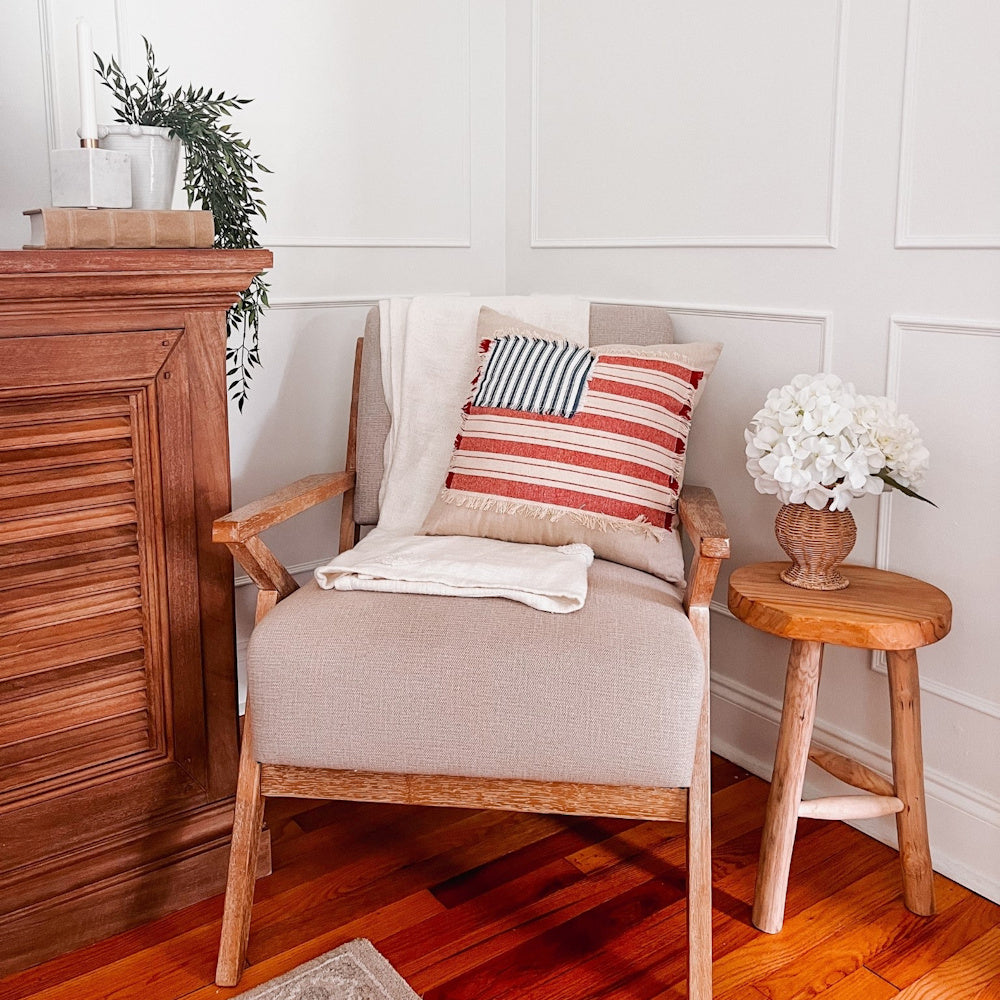 Rustic wood chair with American flag pillow next to a resin basket weave vase and white flowers on a wooden stool.