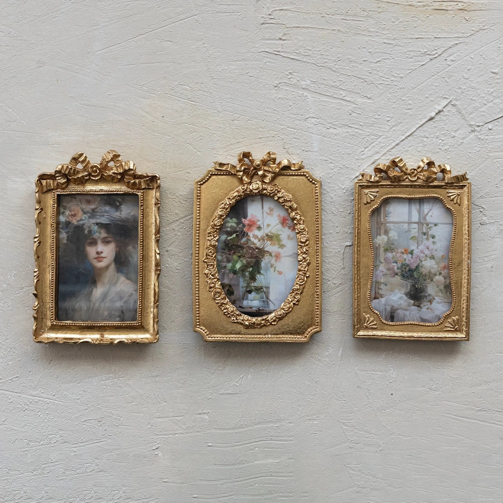 Three ornate gold resin photo frames with bow details and vintage portraits hanging on a textured cream wall.