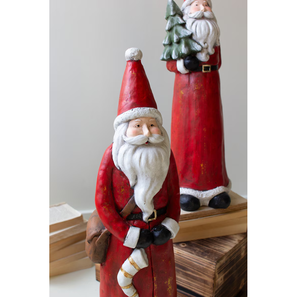 Close-up of two tall resin Santa figurines with red coats and white beards.