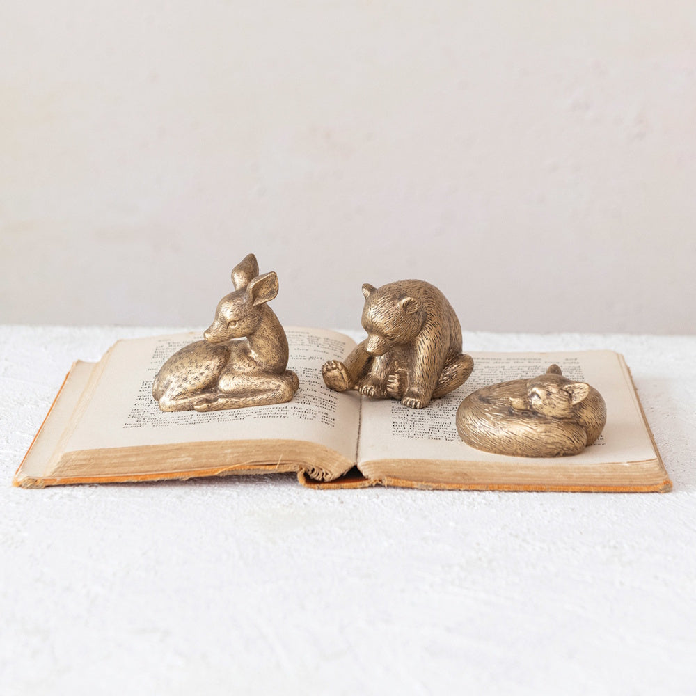 Three small bronze figurines of a deer, bear, and sleeping fox resting on an open vintage book.
