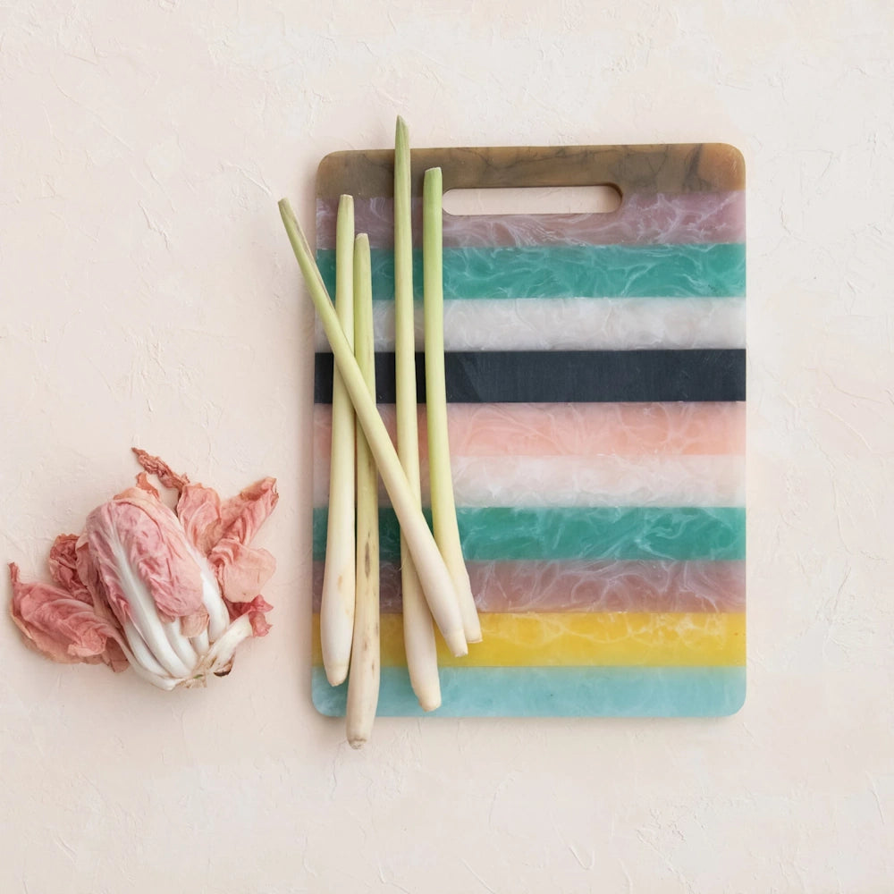 Fresh lemongrass stalks on a colorful striped cutting board next to a pink radicchio head on a light textured surface.