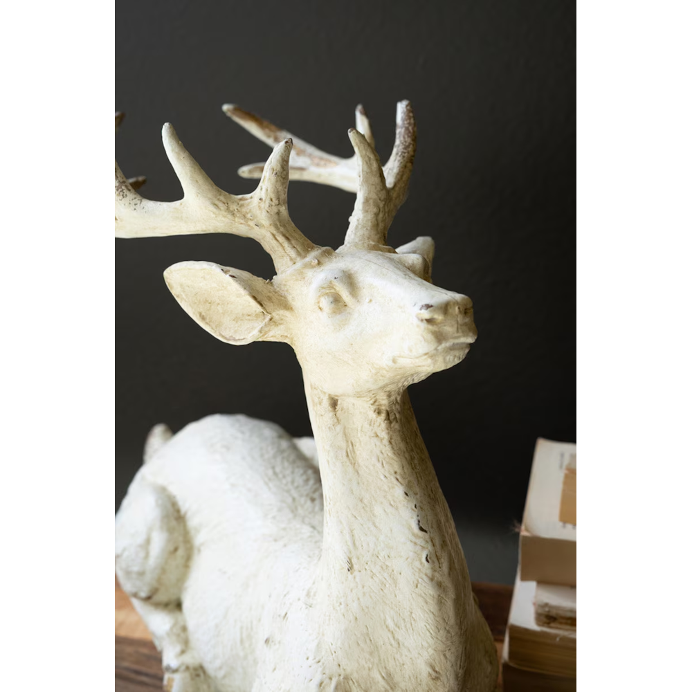 Close-up portrait of a faux-concrete resting deer figurine with antlers.