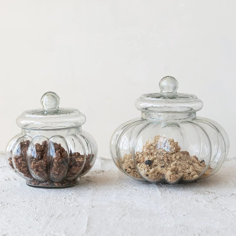 Two ribbed glass jars with lids containing granola and cereal on a white textured surface for kitchen storage.