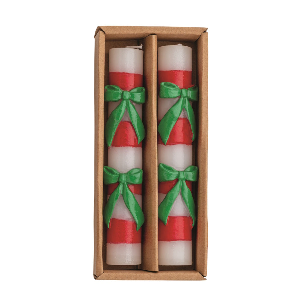 Flat lay view of two white and red striped wax mini taper candles adorned with green bows inside a brown cardboard box.
