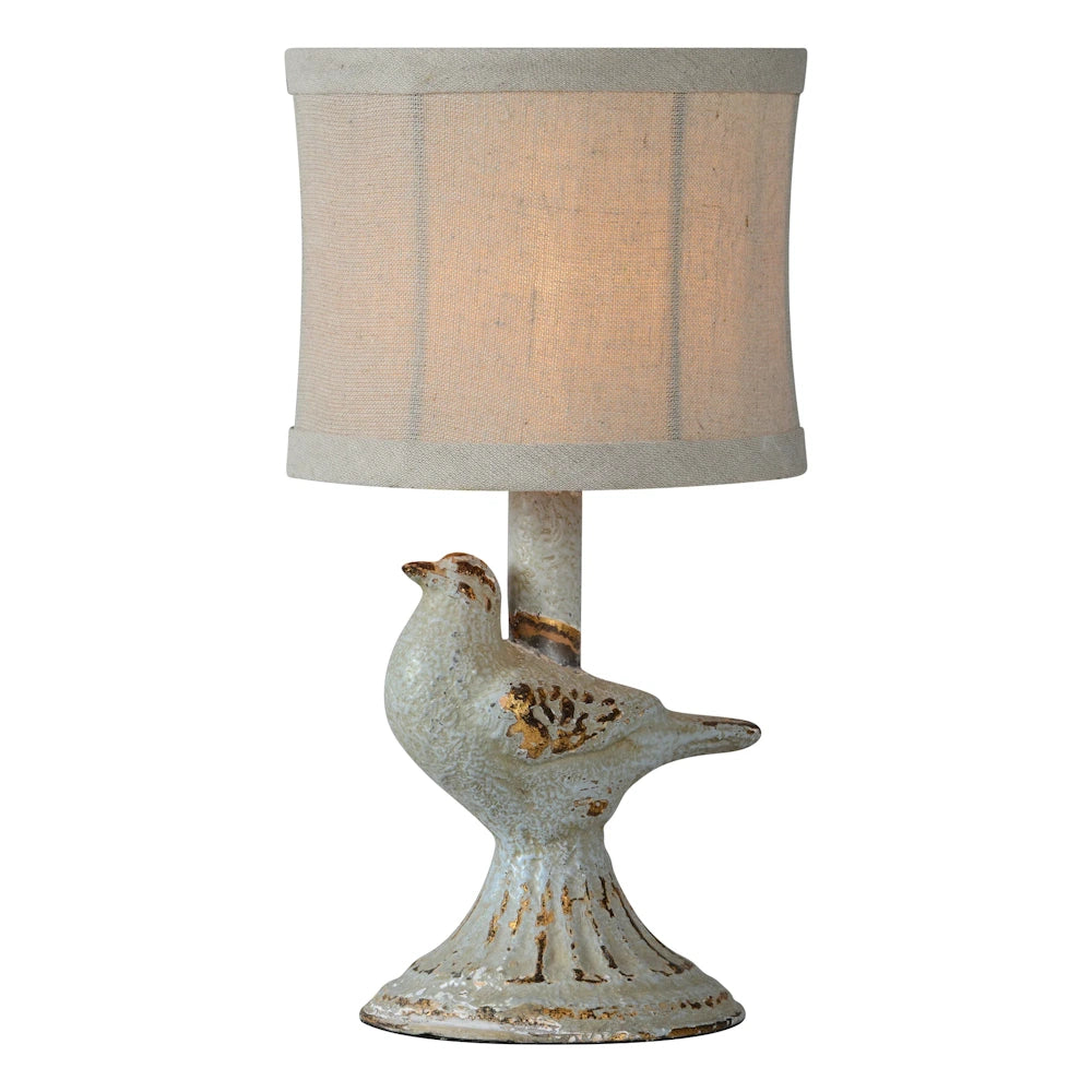 Vintage bird table lamp with distressed white and gold finish and a neutral linen drum shade on a white background.