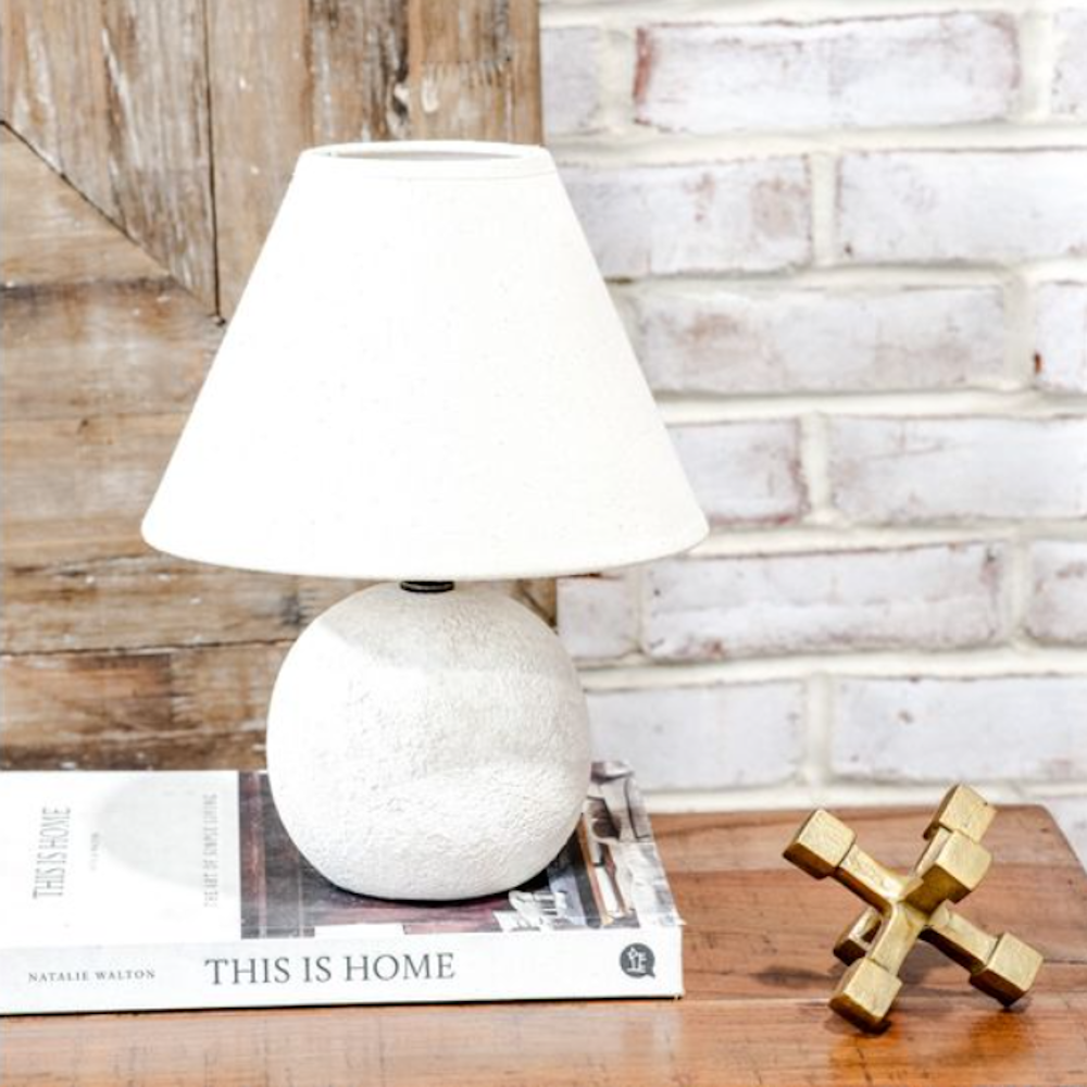 Small white ceramic table lamp with a textured round base and a white fabric tapered shade.
