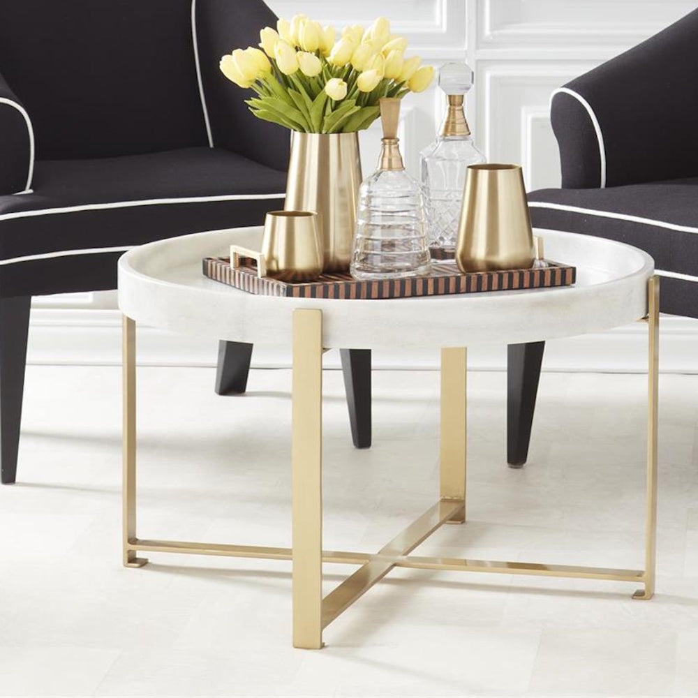 Round white marble coffee table with gold metal cross-base legs, styled with gold vases and yellow flowers.