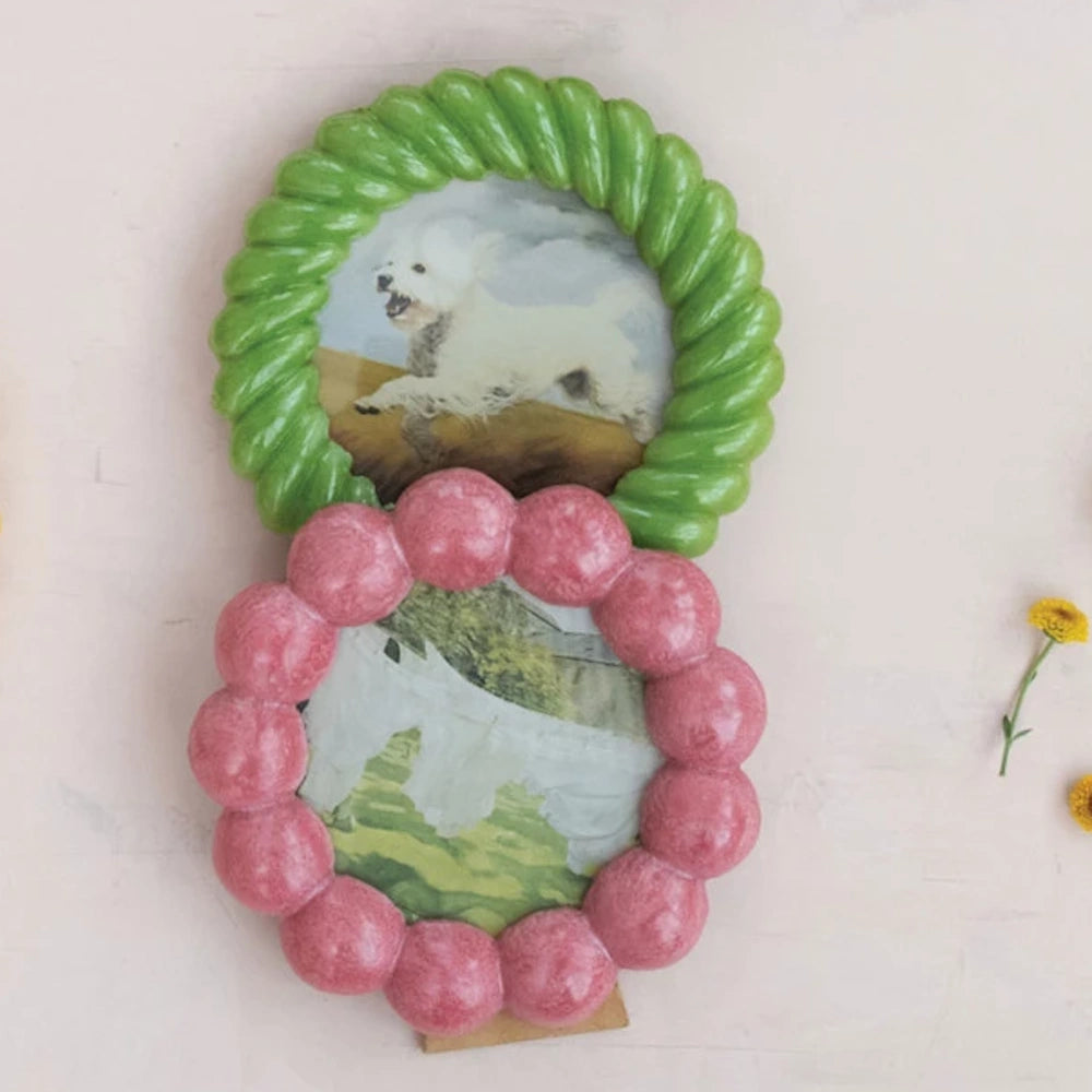 Two round resin photo frames: one green with a rope texture and one pink with a bubble-scalloped border on a white surface.