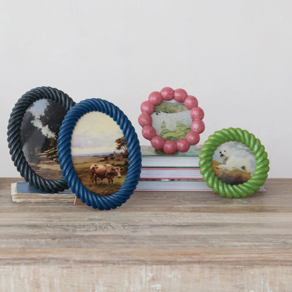 Colorful scalloped and rope-textured resin photo frames in blue, green, and pink displayed on a wooden shelf.