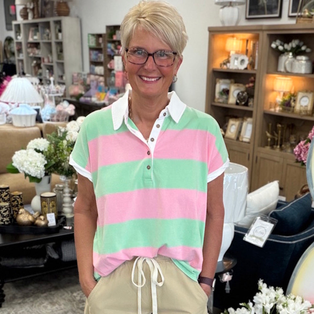 A woman with blonde hair, glasses, and a pink and green striped shirt smiles in a home decor store.
