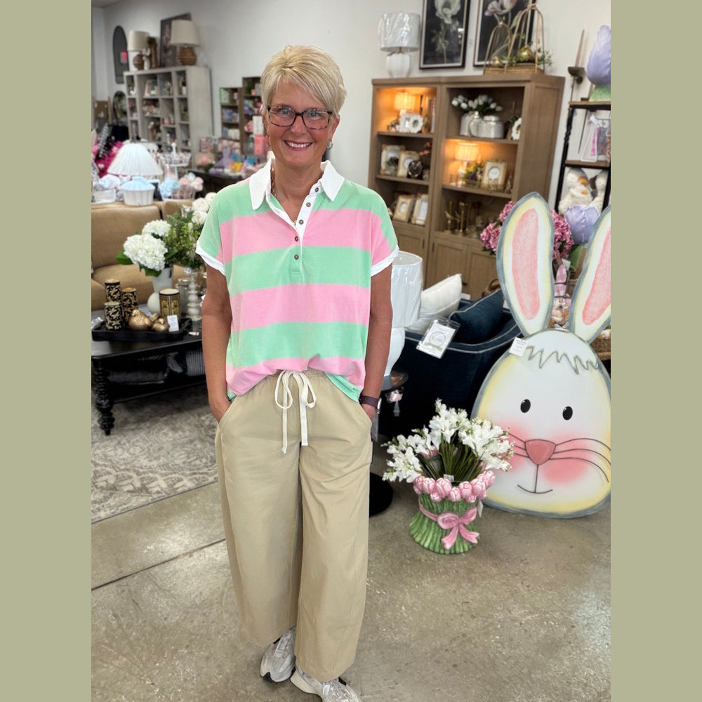 A woman in a pink and mint green striped henley shirt and tan wide-leg pants stands in a gift shop.