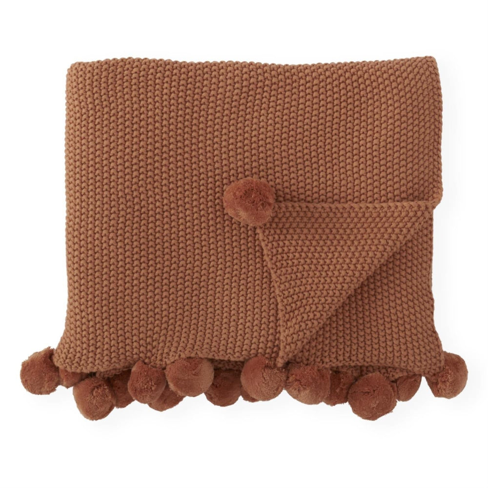 Folded rust-brown knit throw blanket featuring a textured stitch pattern and a decorative pom-pom trim.