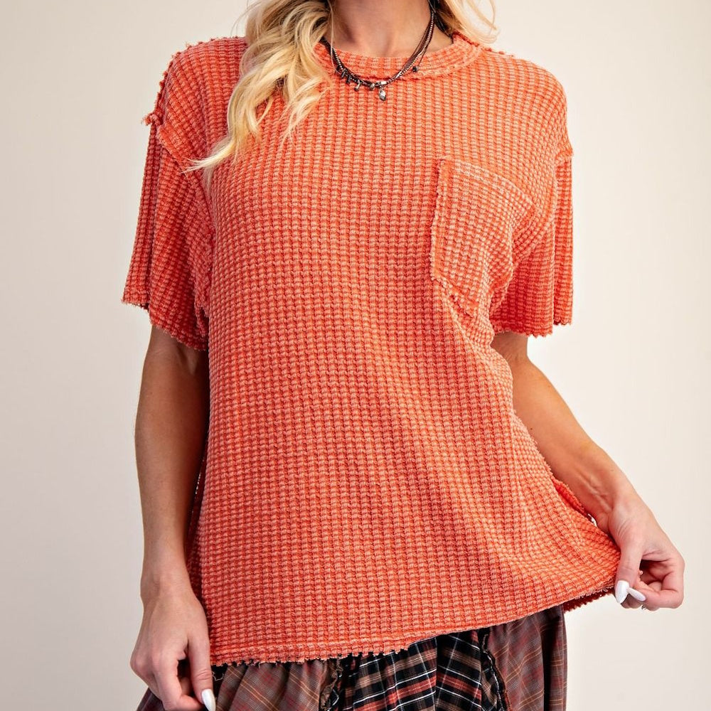 A rust-colored, short-sleeve waffle knit top with a chest pocket, paired with a plaid skirt.