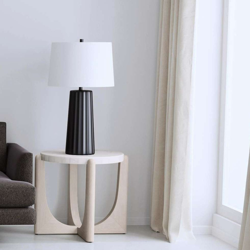 Modern black fluted table lamp on a marble top side table in a bright minimalist living room.