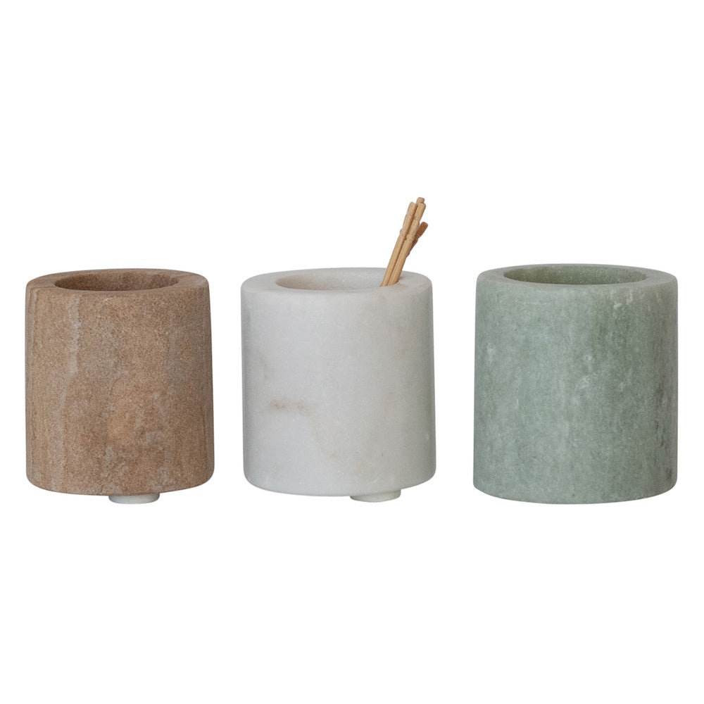 Three small, cylindrical stone toothpick holders in tan, white with wooden toothpicks, and light green.
