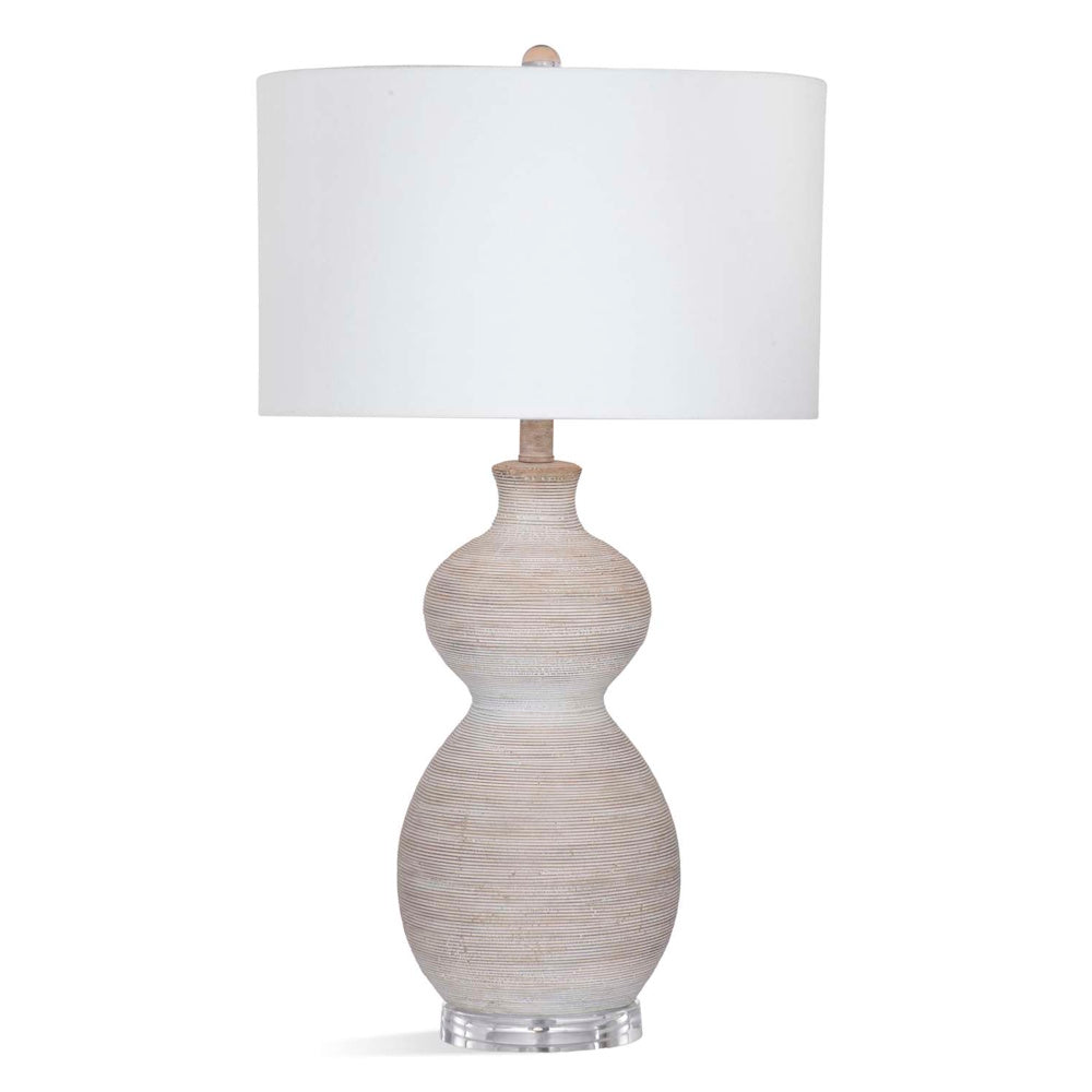 A textured, hourglass-shaped table lamp with a white drum shade and a clear acrylic base.