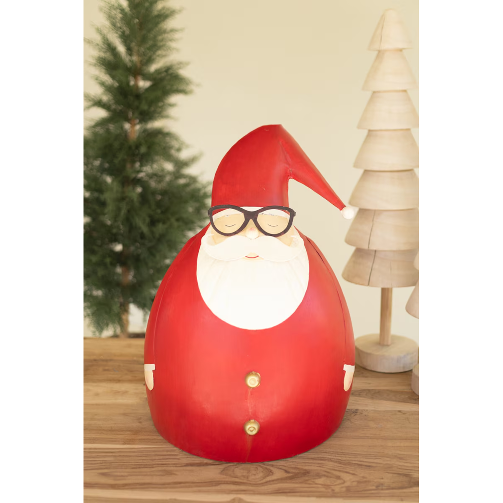 Large painted metal Santa sculpture placed on a wooden table beside Christmas tree decor.