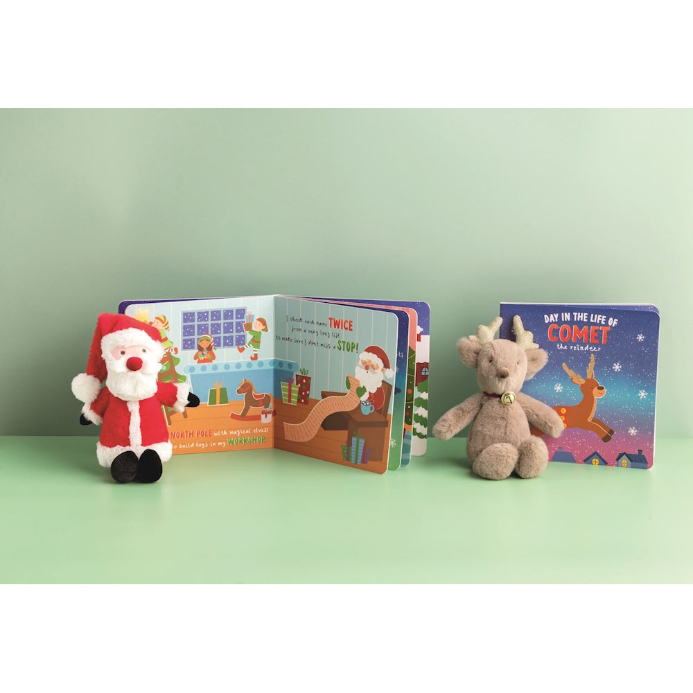 Santa and reindeer plush toys sitting next to open Christmas board books on a green surface.
