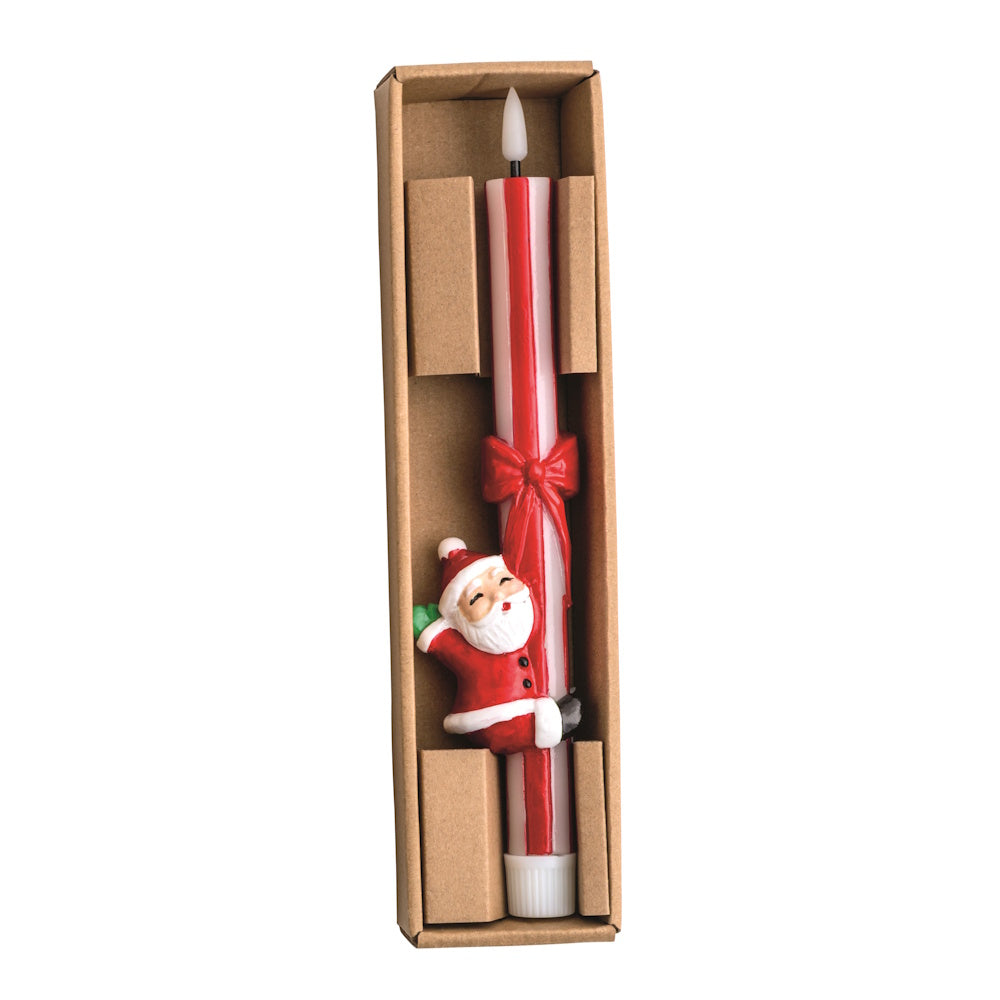 Top-down view of a red and white striped wax taper candle set in a cardboard box, featuring a waving Santa figurine below a red ribbon bow.