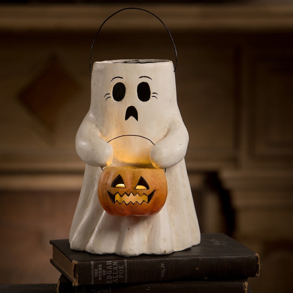 Illuminated ghost lantern holding a jack-o'-lantern bucket, resting on vintage books.