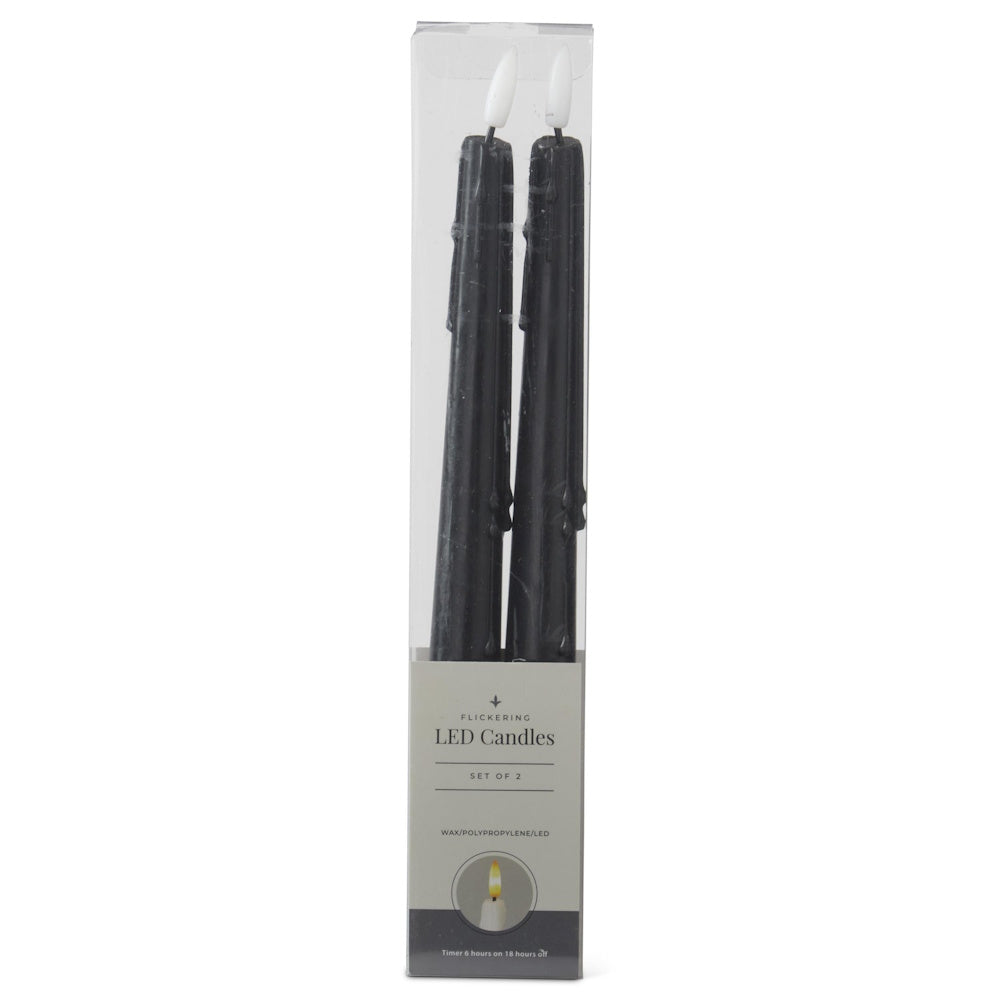 A set of two black flickering LED taper candles with a drip effect in clear plastic packaging.