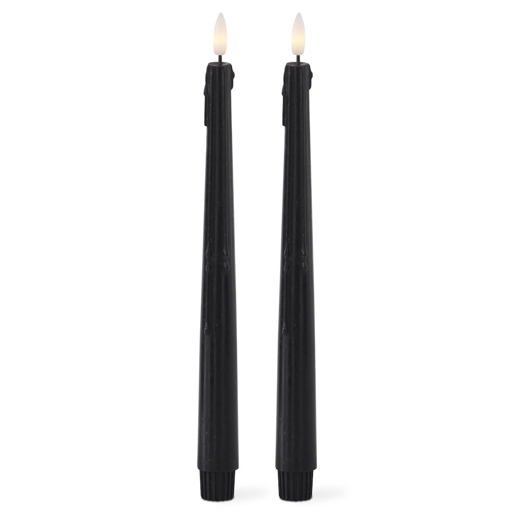 Two tall black flameless taper candles with faux dripping wax and lit LED flames on a white background.