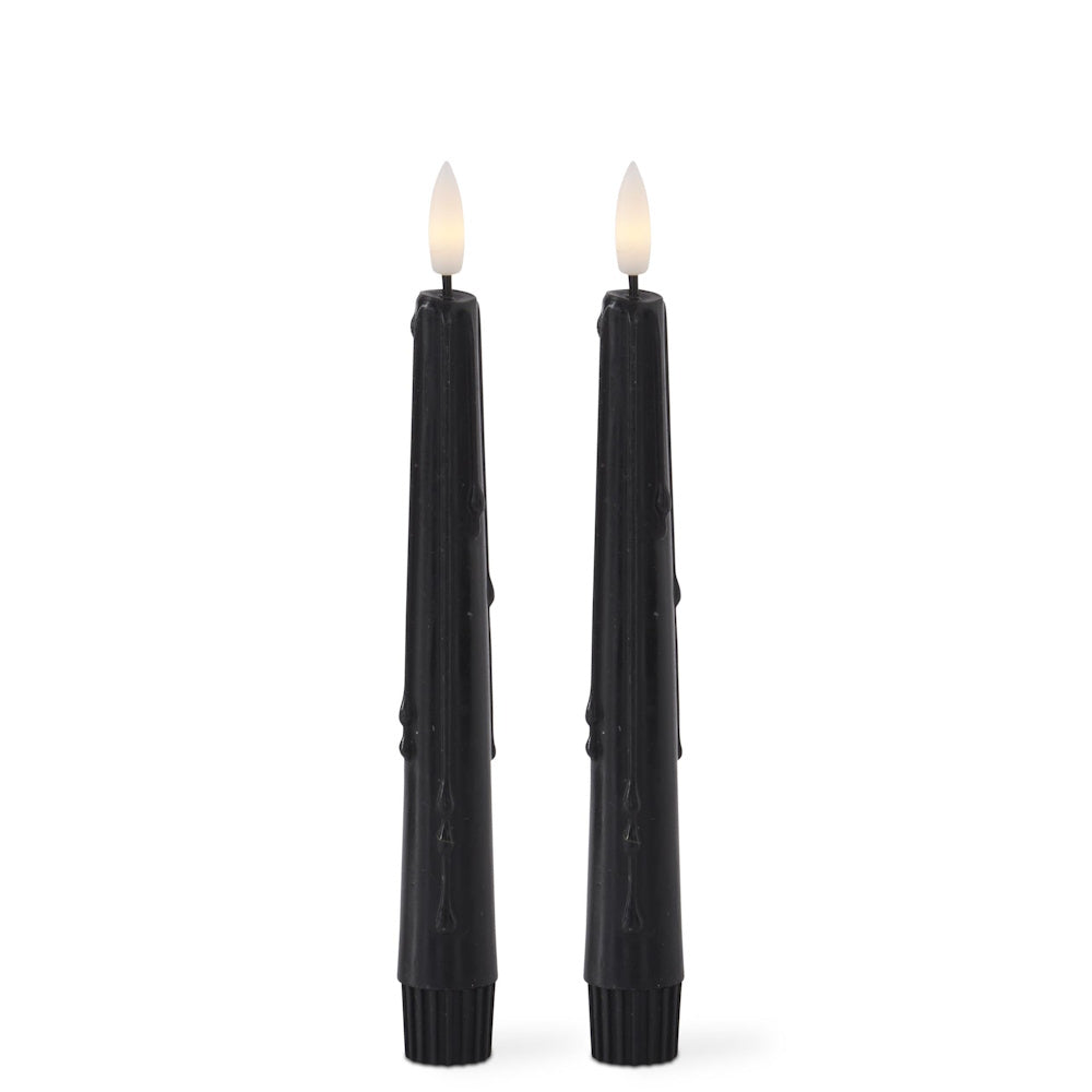 Two tall, black flameless taper candles with faux dripping wax and lit LED flames against a white background.