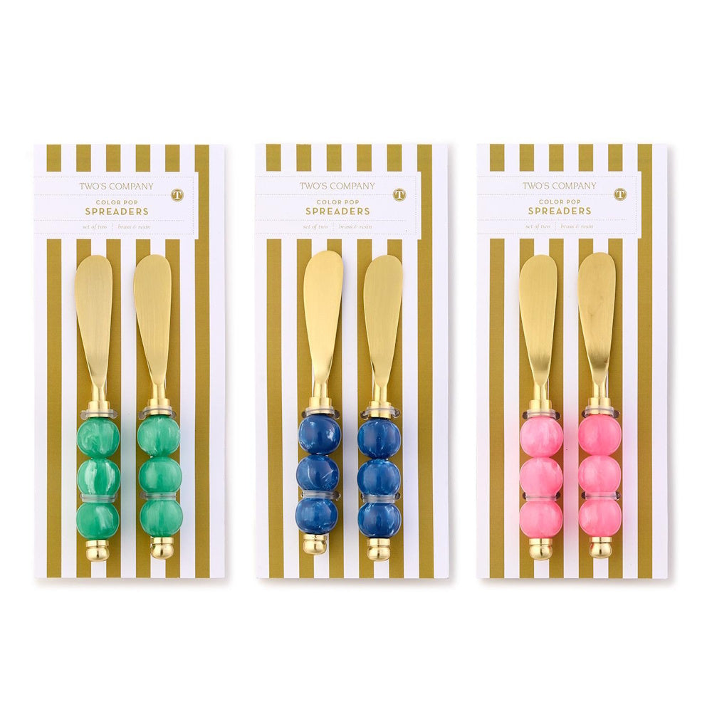 Three sets of Two's Company Color Pop spreaders in green, blue, and pink with beaded handles on card packaging.