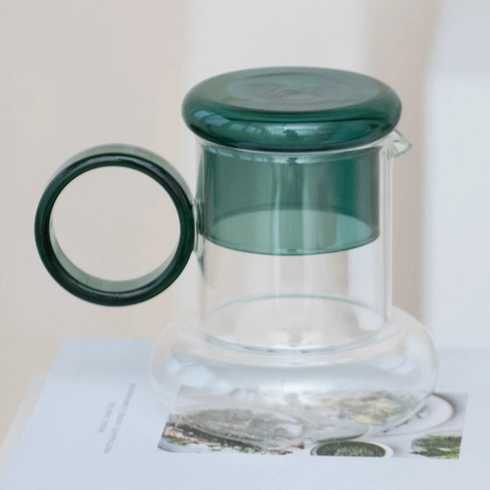 Clear glass pitcher with a wide base, large circular green handle, and a matching green glass lid.