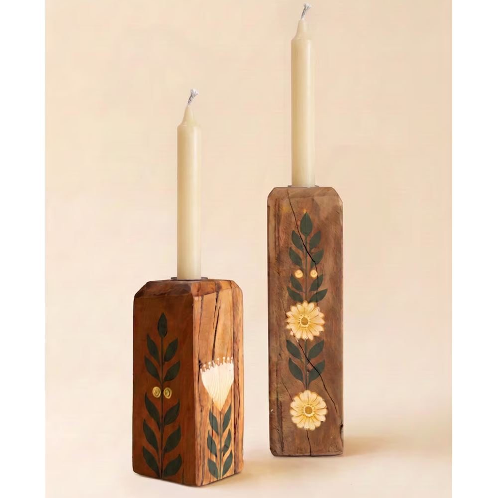 Set of two hand-painted wooden block candle holders with floral motifs and off-white taper candles.