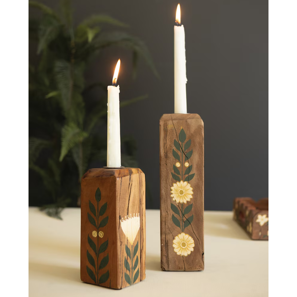 Pair of floral painted wooden candle holders holding lit white tapers against a dark backdrop.
