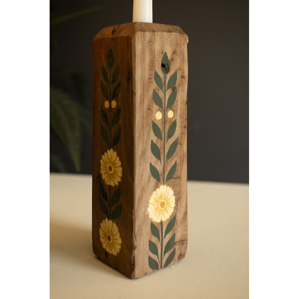 Close-up of a wooden block candle holder hand-painted with yellow flowers and green leafy vines.