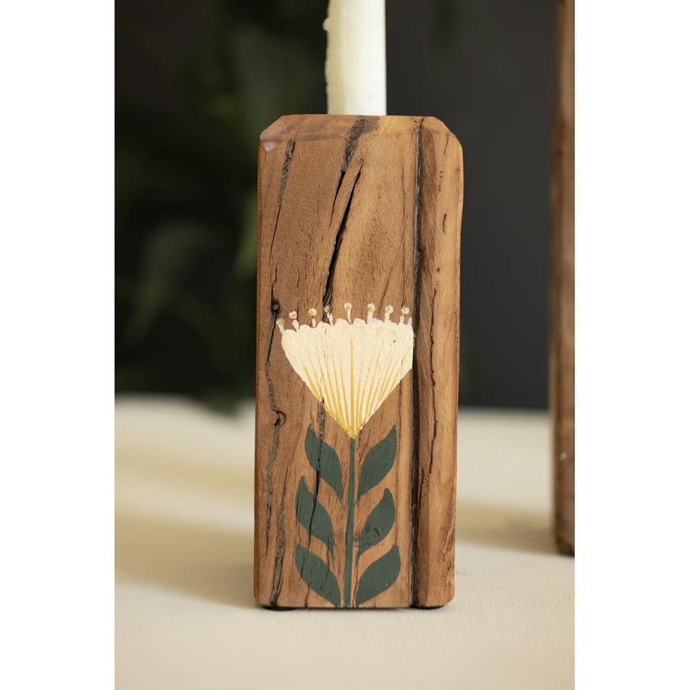 Close-up of a rustic wooden candle holder painted with a yellow fan-shaped flower and green leaves.