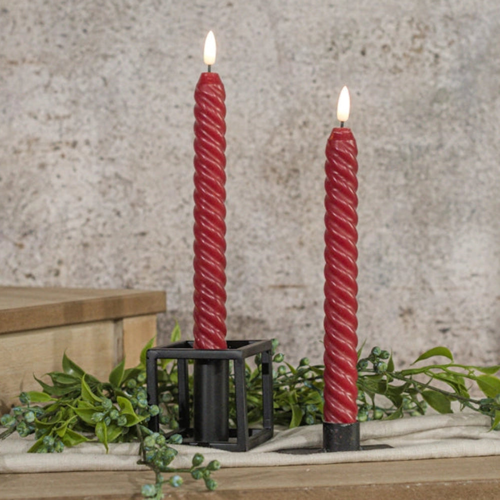 Two red twisted spiral flameless taper candles with lit LED flames in black metal holders.