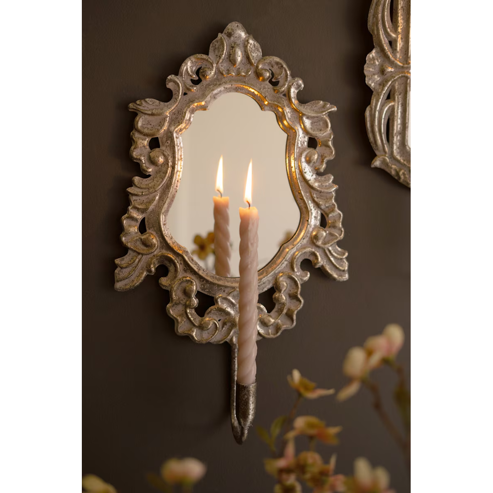 Close-up of an ornate gold mirror wall sconce holding a lit spiral taper candle.