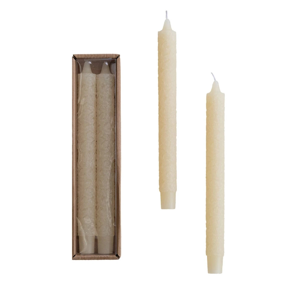 Two ivory unscented taper candles featuring an embossed maple leaf pattern on a white background.