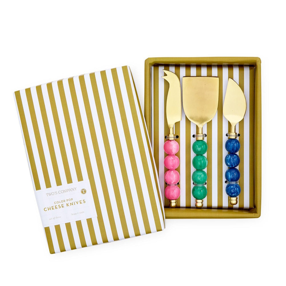 Boxed set of three gold cheese knives with colorful beaded handles beside a striped gift box lid.