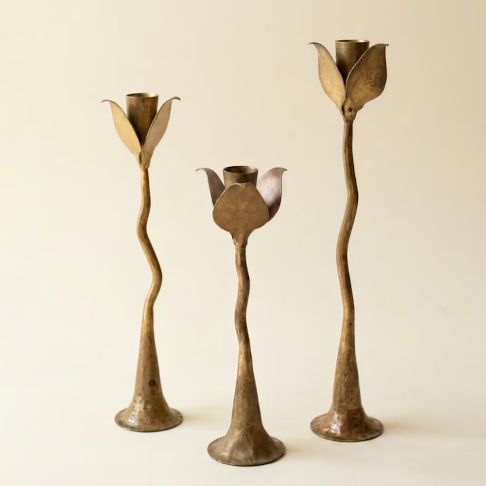 Set of three empty brass forged iron taper candle holders with organic curved stems on beige background.