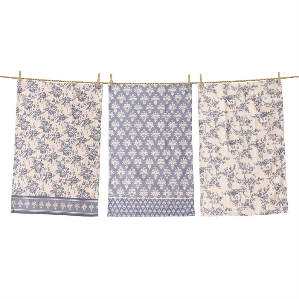 Set of three French blue and white tea towels with floral and damask patterns hanging on a clothesline.