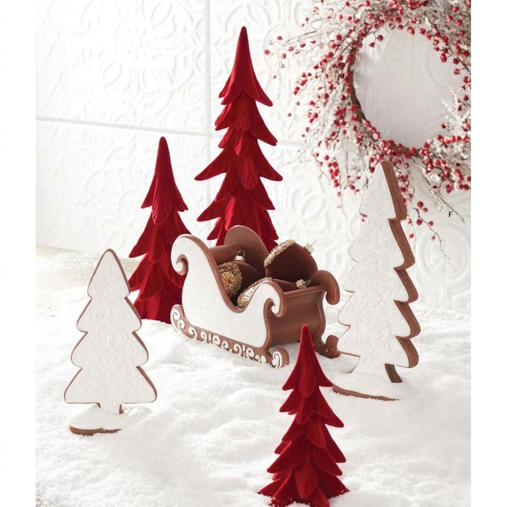 Holiday display featuring red velvet trees, gingerbread sled, white tree cutouts, and a red berry wreath.